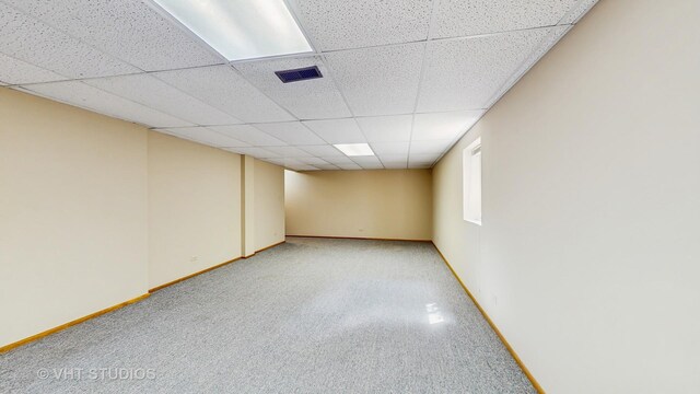below grade area with a drop ceiling, light carpet, and baseboards