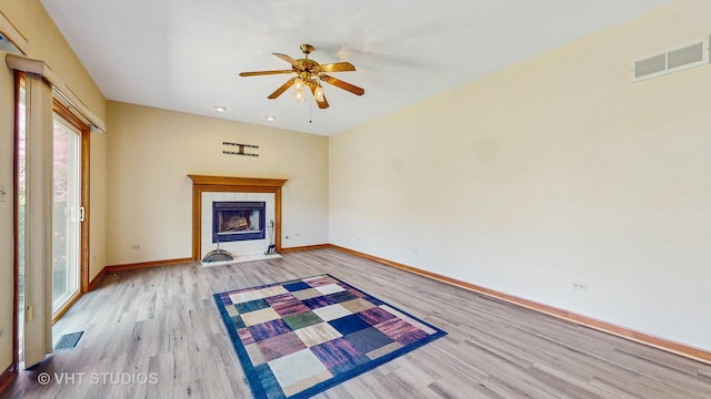 unfurnished living room with wood finished floors, a ceiling fan, baseboards, and a tiled fireplace