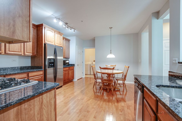 kitchen featuring independent washer and dryer, pendant lighting, appliances with stainless steel finishes, dark stone countertops, and light wood finished floors