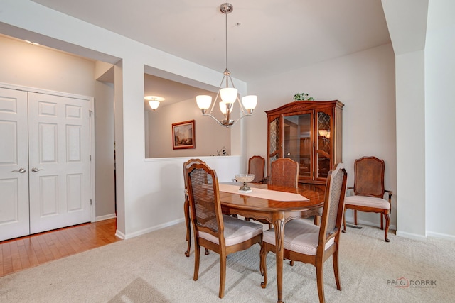 dining space with baseboards, light colored carpet, and a notable chandelier