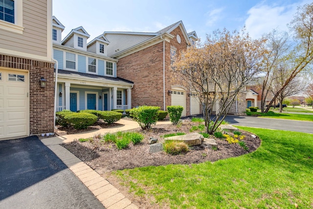 view of side of property featuring aphalt driveway, brick siding, an attached garage, a yard, and a porch