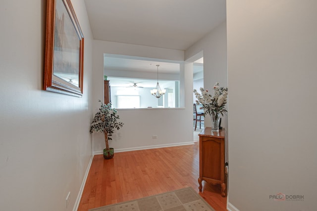 hallway featuring baseboards, a notable chandelier, and wood finished floors
