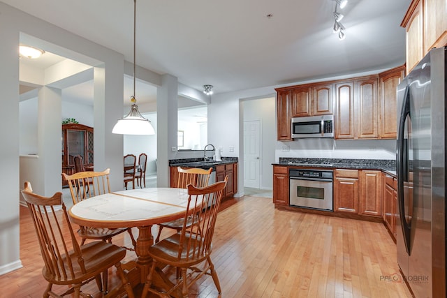 kitchen with appliances with stainless steel finishes, a sink, light wood finished floors, brown cabinetry, and decorative light fixtures