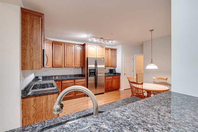 kitchen featuring pendant lighting, appliances with stainless steel finishes, a sink, dark stone countertops, and light wood-style floors