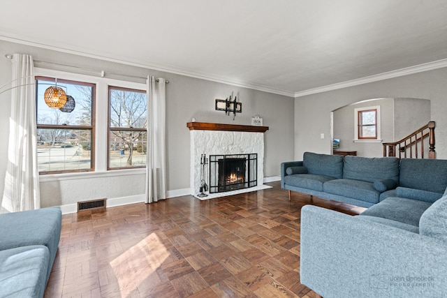 living room featuring a fireplace with flush hearth, arched walkways, baseboards, ornamental molding, and visible vents