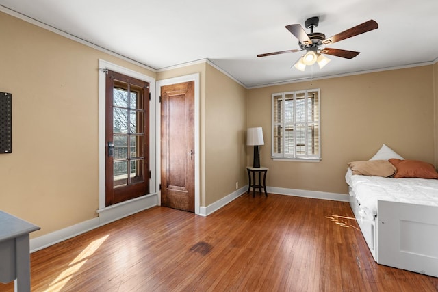 bedroom featuring wood-type flooring, baseboards, crown molding, and multiple windows