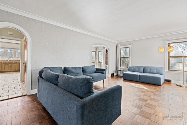 living room featuring arched walkways, visible vents, baseboards, and ornamental molding