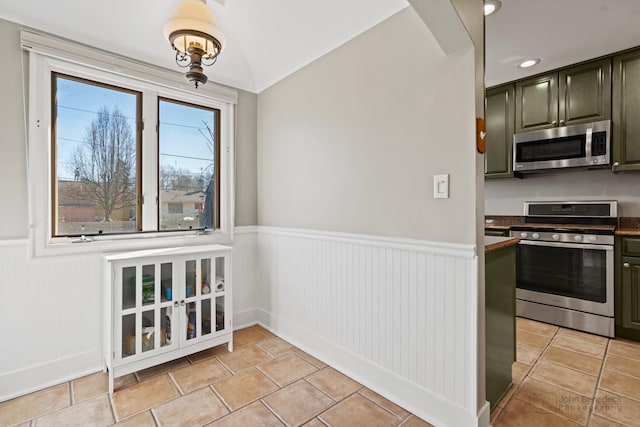 kitchen featuring wainscoting, stainless steel appliances, lofted ceiling, and dark countertops