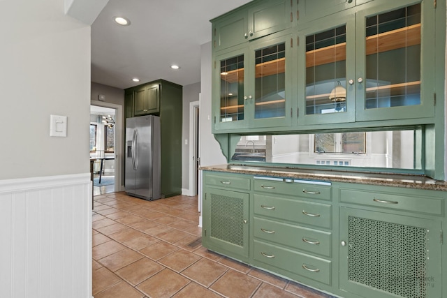 kitchen featuring a wainscoted wall, green cabinetry, light tile patterned flooring, stainless steel fridge, and glass insert cabinets
