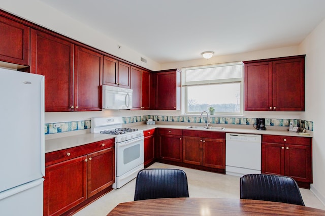 kitchen featuring light countertops, white appliances, a sink, and reddish brown cabinets