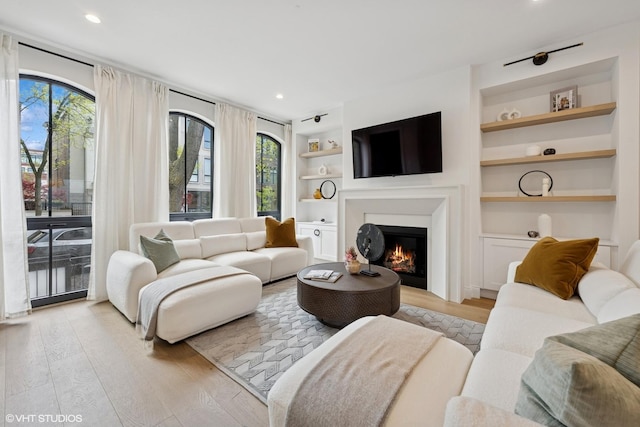living area featuring built in features, light wood finished floors, a warm lit fireplace, and recessed lighting