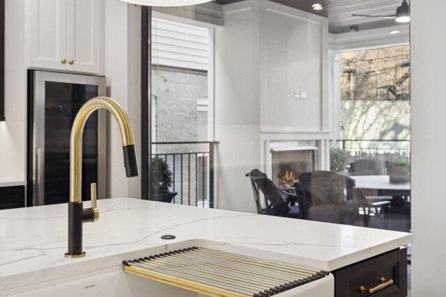 kitchen featuring light stone countertops, white cabinets, a sink, a lit fireplace, and ceiling fan
