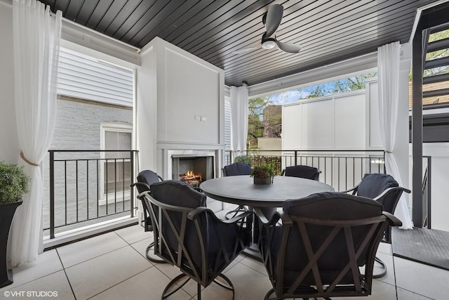 view of patio / terrace with a lit fireplace, outdoor dining area, and ceiling fan