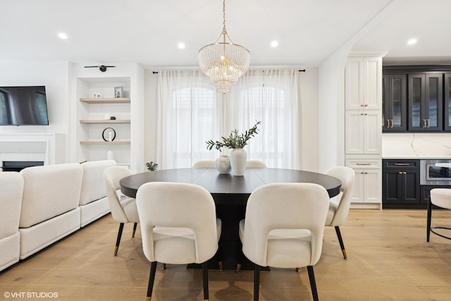 dining area featuring a chandelier, light wood-style flooring, built in shelves, recessed lighting, and a fireplace