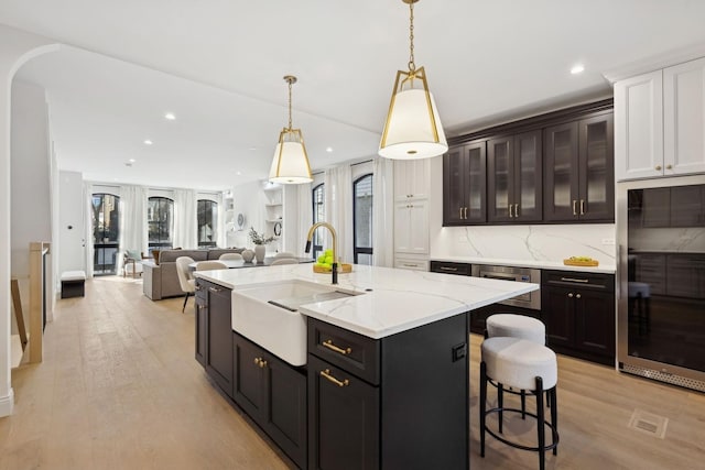 kitchen featuring a sink, light wood-style flooring, backsplash, a center island with sink, and light stone counters