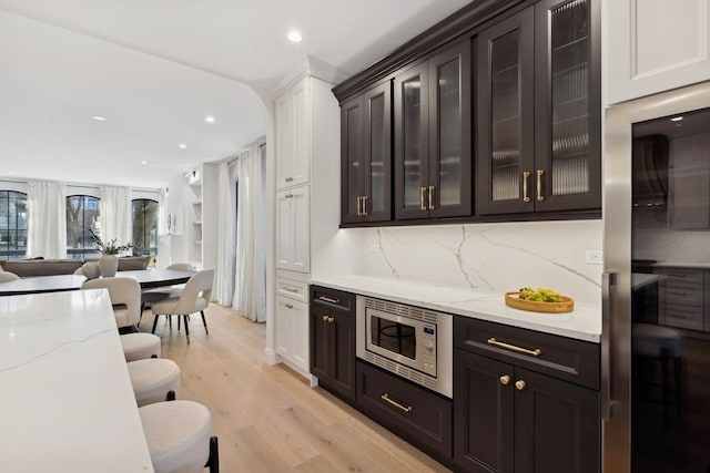 bar area featuring stainless steel microwave, light wood finished floors, decorative backsplash, and recessed lighting