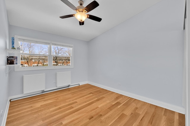 unfurnished room featuring radiator, wood finished floors, a ceiling fan, and baseboards