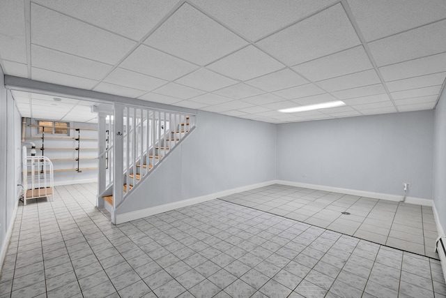 finished below grade area featuring stairway, tile patterned flooring, a drop ceiling, baseboards, and a baseboard radiator