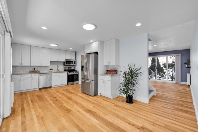 kitchen with decorative backsplash, light wood finished floors, white cabinets, baseboards, and appliances with stainless steel finishes