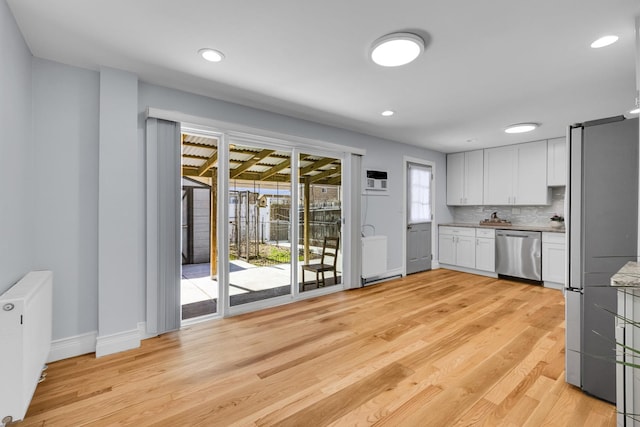 kitchen with white cabinets, radiator, light wood-style flooring, tasteful backsplash, and appliances with stainless steel finishes