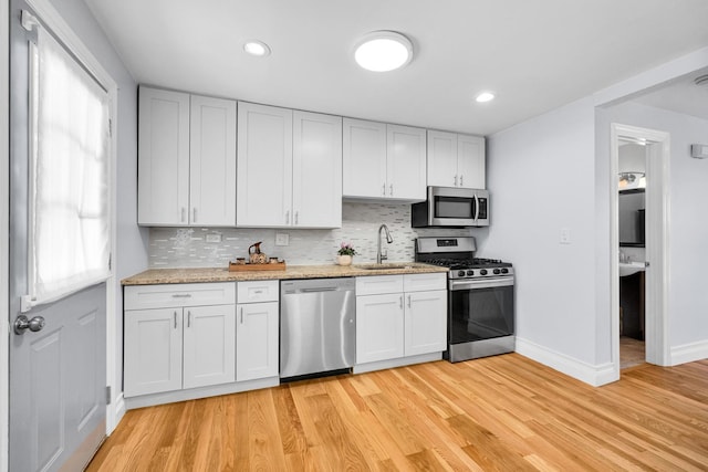 kitchen with light wood-style floors, tasteful backsplash, stainless steel appliances, and a sink