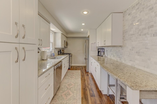 kitchen with dark wood-style floors, a sink, tasteful backsplash, appliances with stainless steel finishes, and white cabinetry
