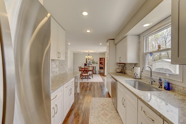 kitchen with a sink, white cabinetry, a chandelier, decorative backsplash, and appliances with stainless steel finishes