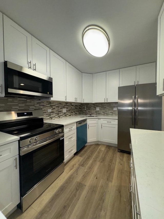 kitchen featuring stainless steel appliances, a sink, light wood-style flooring, backsplash, and light countertops