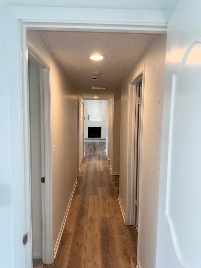 hallway with hardwood / wood-style floors, baseboards, recessed lighting, and a textured ceiling