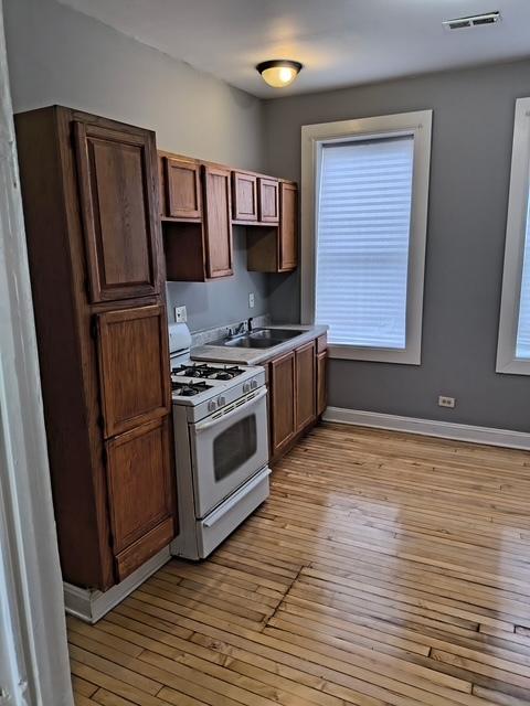 kitchen with a sink, white range with gas stovetop, light wood-style floors, baseboards, and visible vents