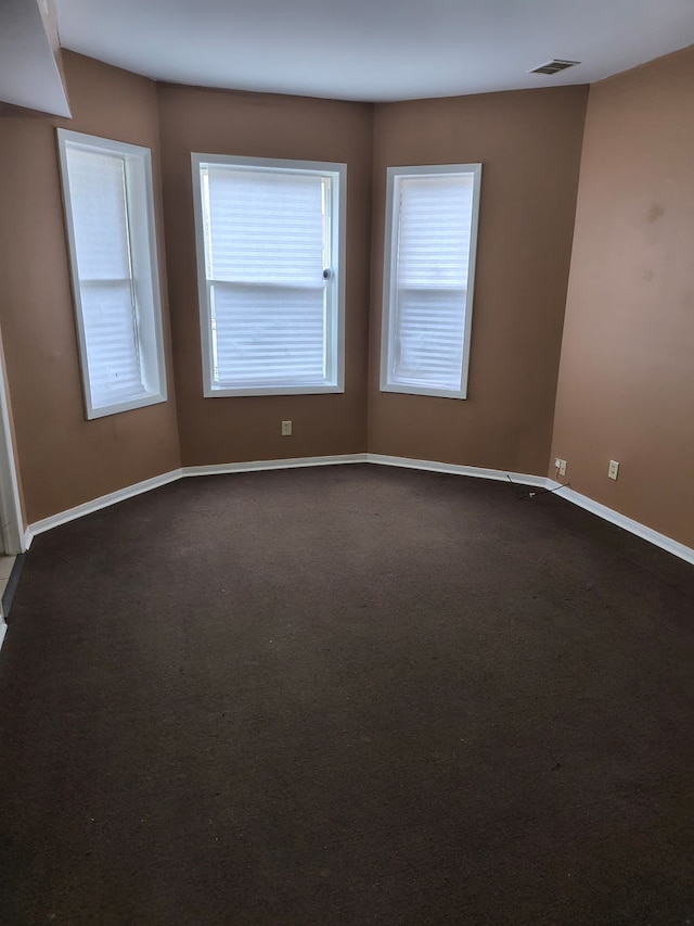 unfurnished room with baseboards, dark colored carpet, and visible vents