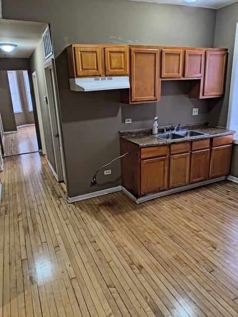 kitchen with brown cabinets, dark countertops, light wood-type flooring, and a sink