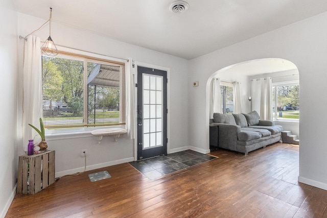 foyer entrance featuring visible vents, arched walkways, dark wood finished floors, and baseboards