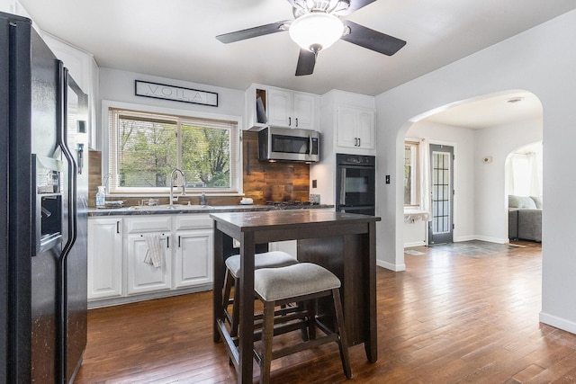 kitchen with white cabinets, black fridge, a sink, arched walkways, and stainless steel microwave