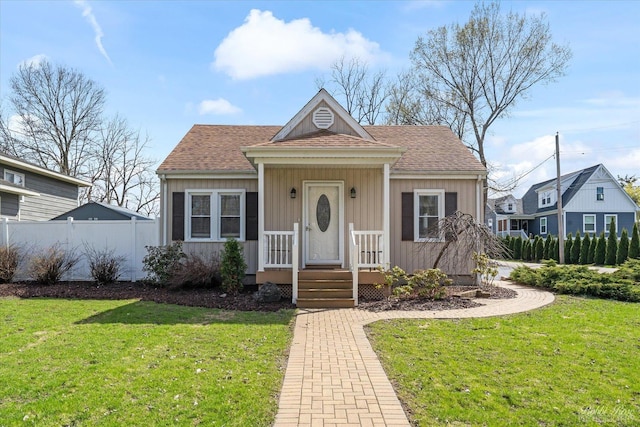 bungalow featuring fence, a shingled roof, and a front yard