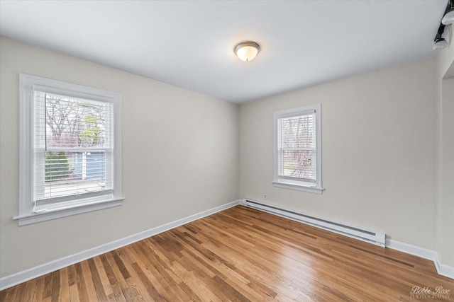 empty room featuring a baseboard radiator, wood finished floors, a healthy amount of sunlight, and baseboards