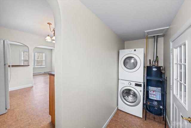 washroom featuring baseboard heating, arched walkways, water heater, stacked washer and dryer, and laundry area