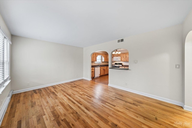 unfurnished living room featuring arched walkways, light wood-style floors, a healthy amount of sunlight, and baseboard heating