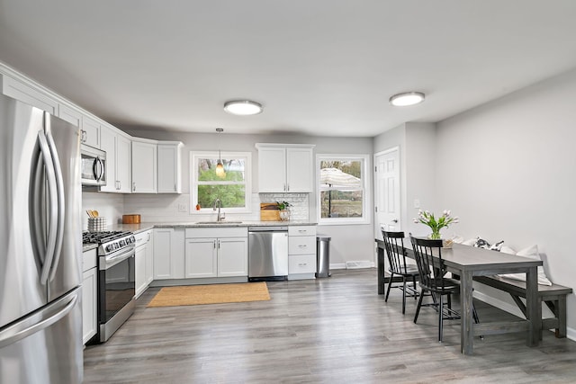 kitchen featuring stainless steel appliances, backsplash, wood finished floors, a sink, and white cabinetry