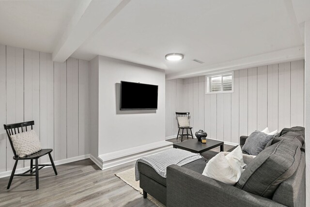 living area with wood walls, wood finished floors, beamed ceiling, baseboards, and visible vents