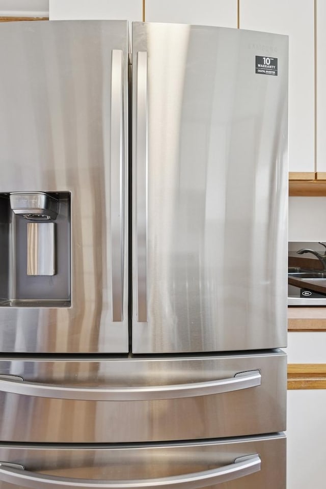 room details with stainless steel fridge, white cabinets, and a sink