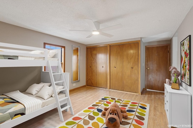 bedroom with a ceiling fan, two closets, light wood finished floors, and a textured ceiling