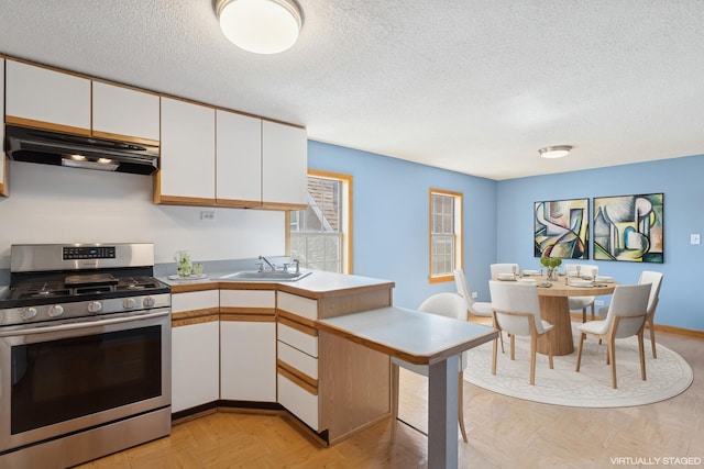 kitchen featuring a textured ceiling, stainless steel range with gas stovetop, a sink, under cabinet range hood, and white cabinetry