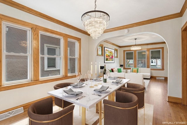 dining area with crown molding, an inviting chandelier, light wood-style floors, arched walkways, and visible vents