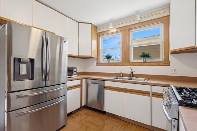 kitchen with track lighting, a sink, light countertops, stainless steel appliances, and white cabinetry
