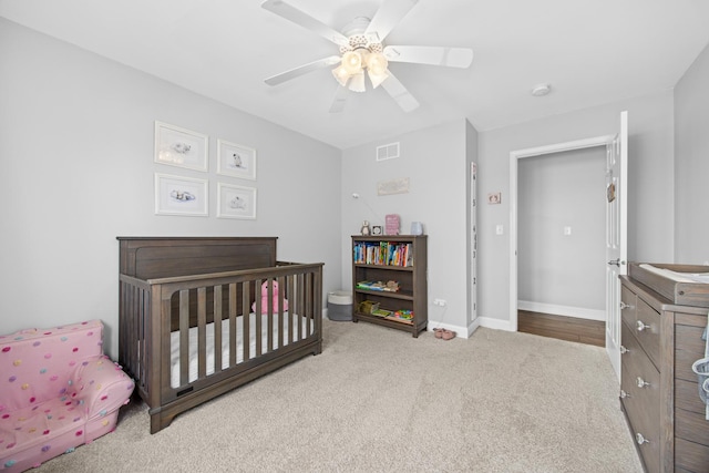 carpeted bedroom with a ceiling fan, baseboards, visible vents, and a nursery area