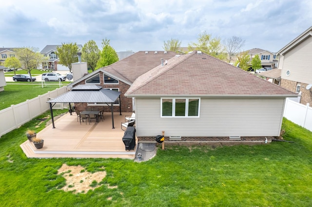back of property with a shingled roof, a gazebo, a wooden deck, a fenced backyard, and a lawn