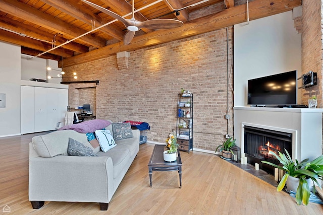 living area with a fireplace with flush hearth, a ceiling fan, wooden ceiling, beamed ceiling, and baseboards