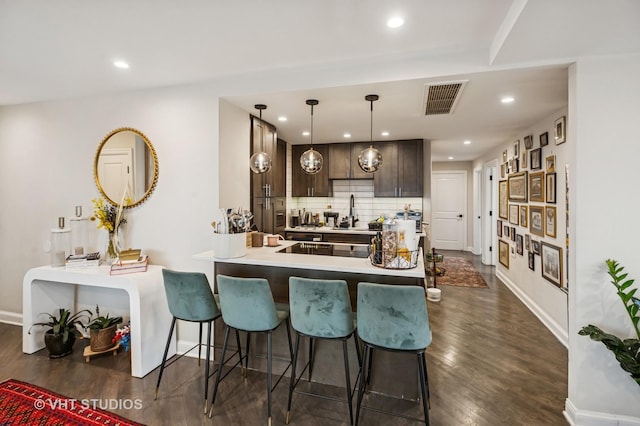 kitchen with a breakfast bar area, visible vents, dark wood finished floors, baseboards, and dark brown cabinets