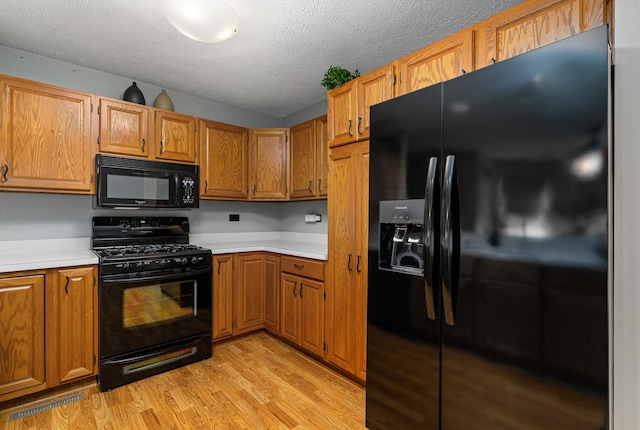 4232 Caribou Ct, Joliet, IL 60431 - kitchen with black appliances, light countertops, light wood-style floors, a textured ceiling, and brown cabinets